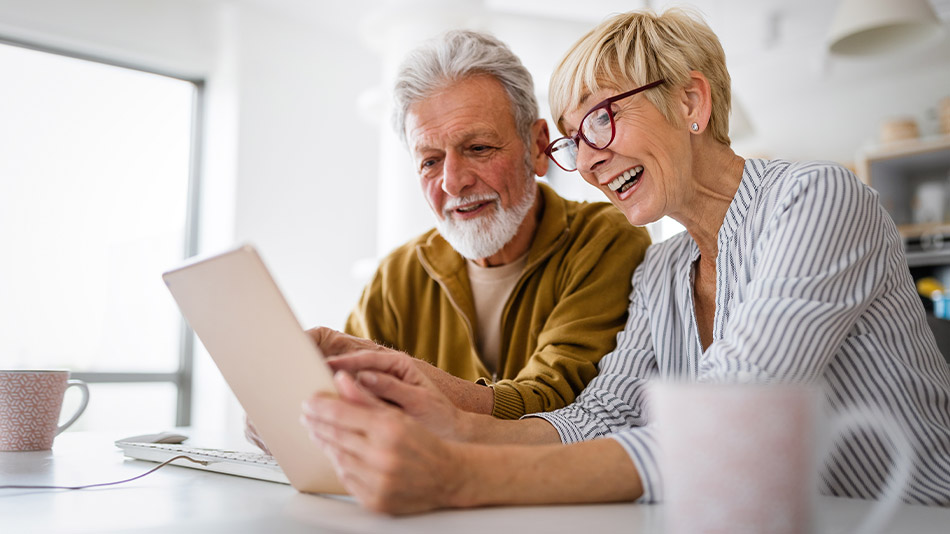 A senior couple with glasses looking at an iPad in their kitchen.
