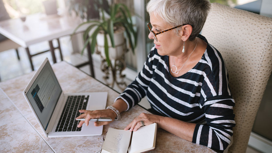 A middle-aged woman with short hair looking at her computer, researching whether refractive lens exchange is covered by insurance.